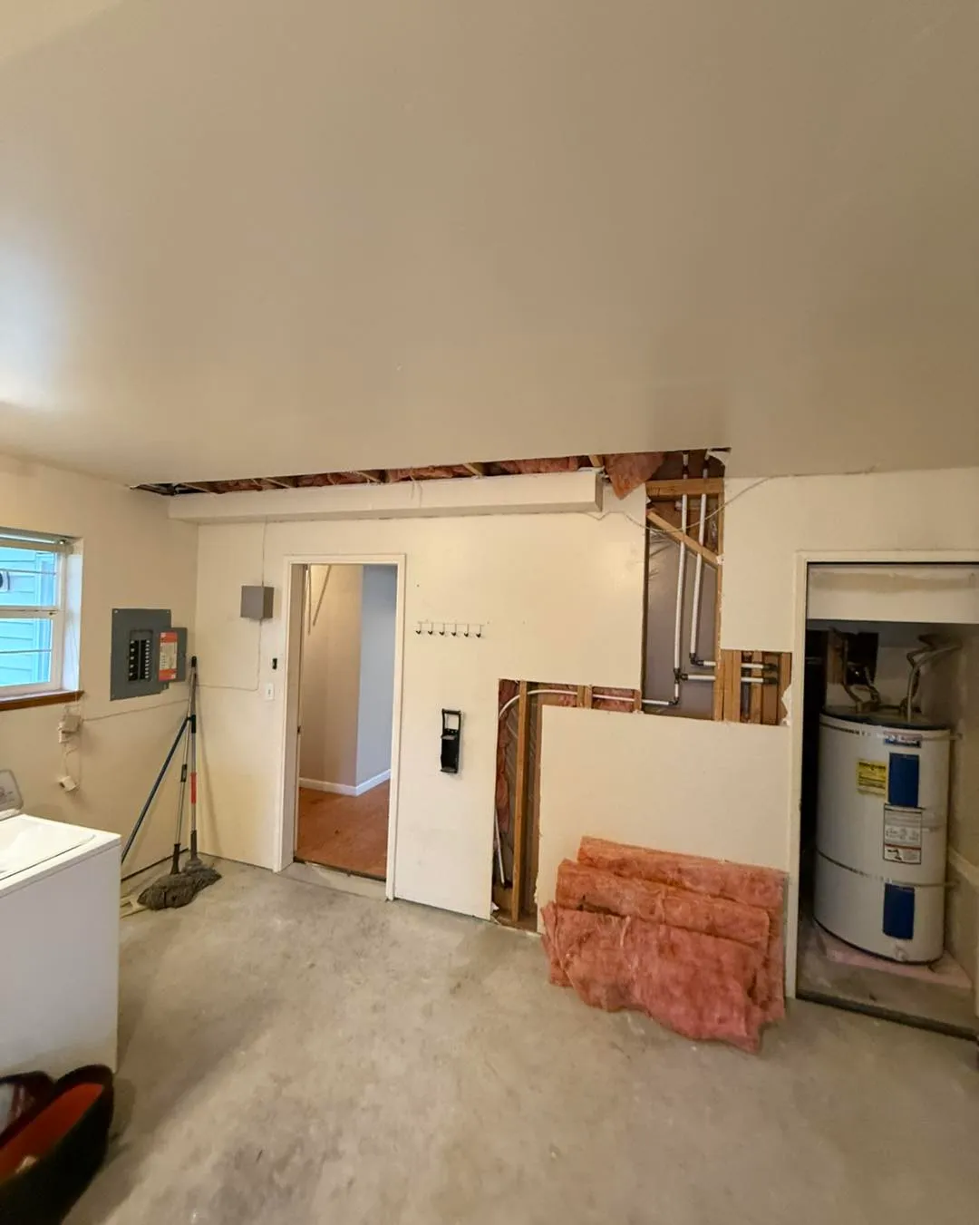 Basement utility room with ceiling and wall sections removed for pipe access near water heater
