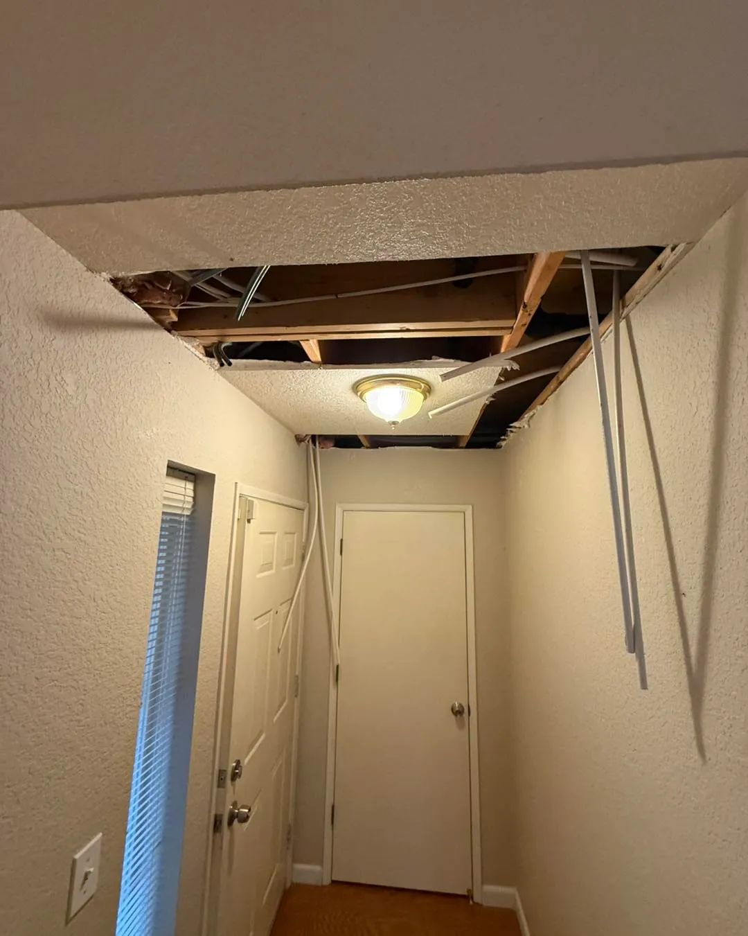 Hallway ceiling cut open with large rectangular hole exposing framing and pipe runs